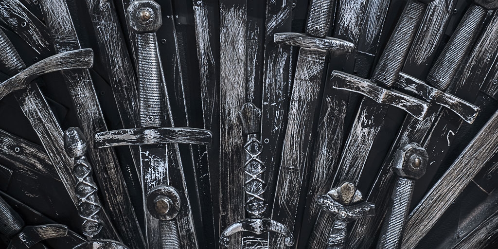 Close-up view of a metallic throne constructed from an array of swords. The swords' intricate, spiky arrangement mirrors the rise of streaming content providers, where complexity grows along with costs, showcasing a medieval, artistic design. The metal appears worn and weathered.