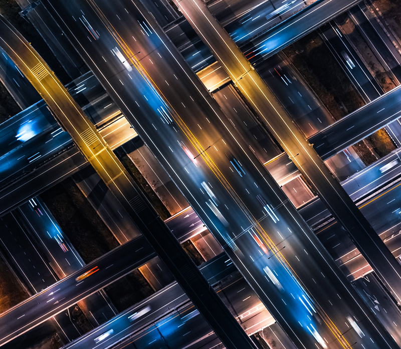 Aerial view of an illuminated, multi-level highway interchange at night. Cars create streaks of light on the roads, highlighting the intricate network of lanes and overpasses in a geometric pattern—a scene reminiscent of a Custom 400G from Uniti Wholesale's seamless connectivity.