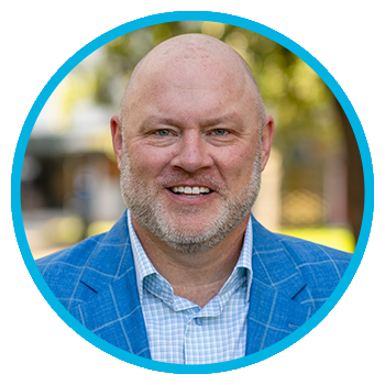 Meet Uniti Wholesale: A smiling bald man with a light beard wears a blue plaid suit jacket and light shirt, posed outdoors with a blurred background and a blue circular border around the image.